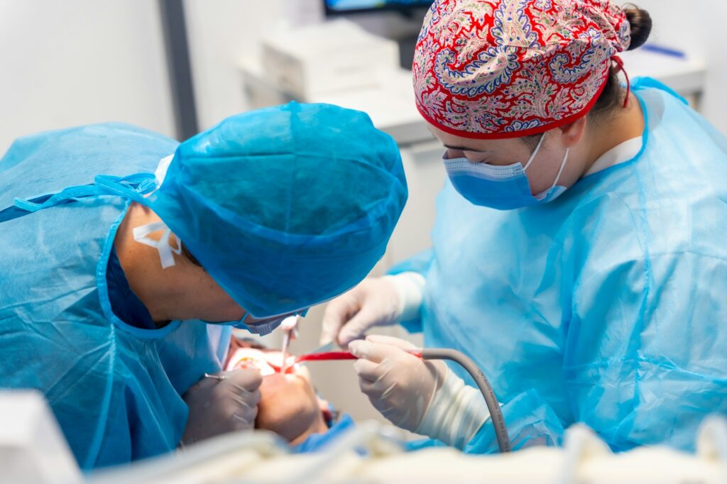 Dental clinic, women dentists in blue suits and hats performing an oral operation