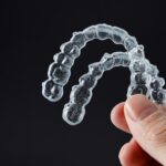 Hand holding two transparent retainers on black background. Invisalign orthodontics concept