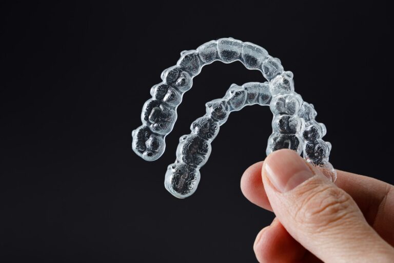 Hand holding two transparent retainers on black background. Invisalign orthodontics concept