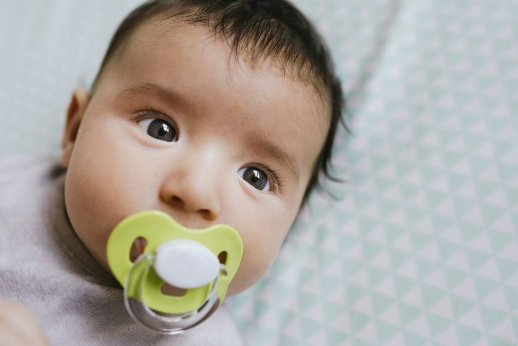 Portrait of baby girl lying on bed sucking a pacifier