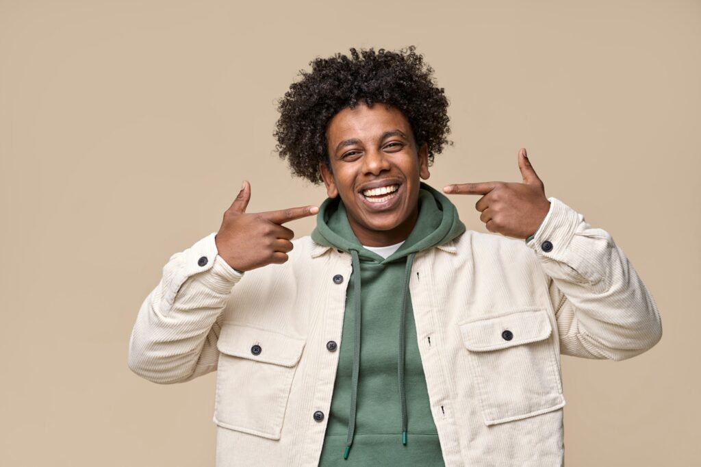 Smiling African guy pointing at dental white teeth advertising whitening.